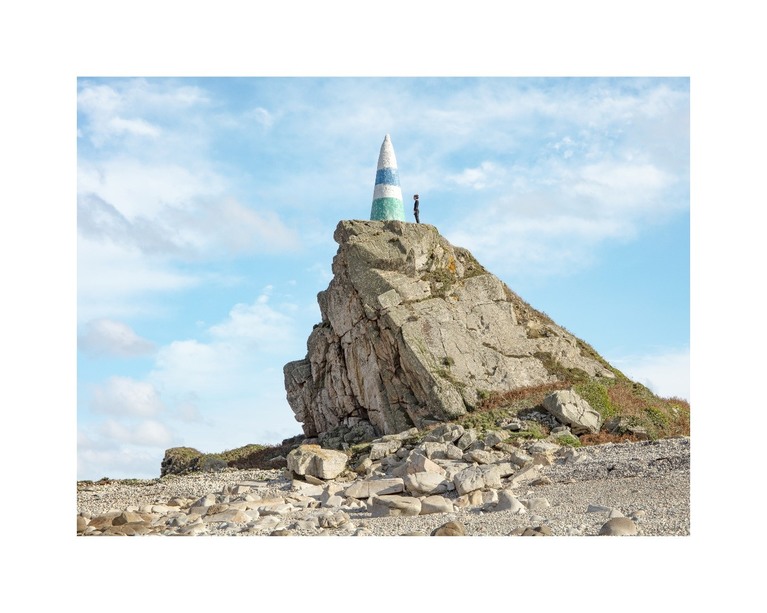 Photo d'un rocher surplombant le littoral de la côte bretonne. Une femme se tient sur le rocher, face à la mer. 
