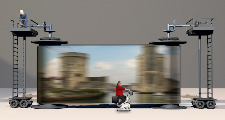 Une femme faisant du vélo d'appartement devant un écran, manipulé par un technicien, où défile l'image des tours de La Rochelle